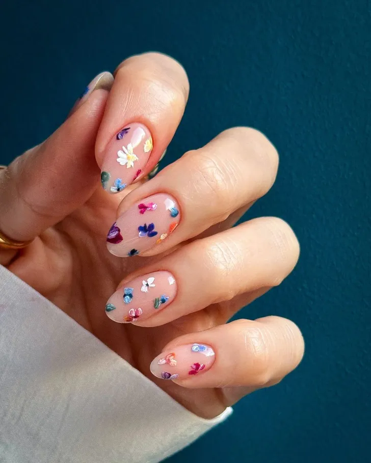 White floral nails with elegant colorful flower designs - classic hand showcasing white base with vibrant colorful flower petals, featuring green leaves and stems on almond-shaped nails